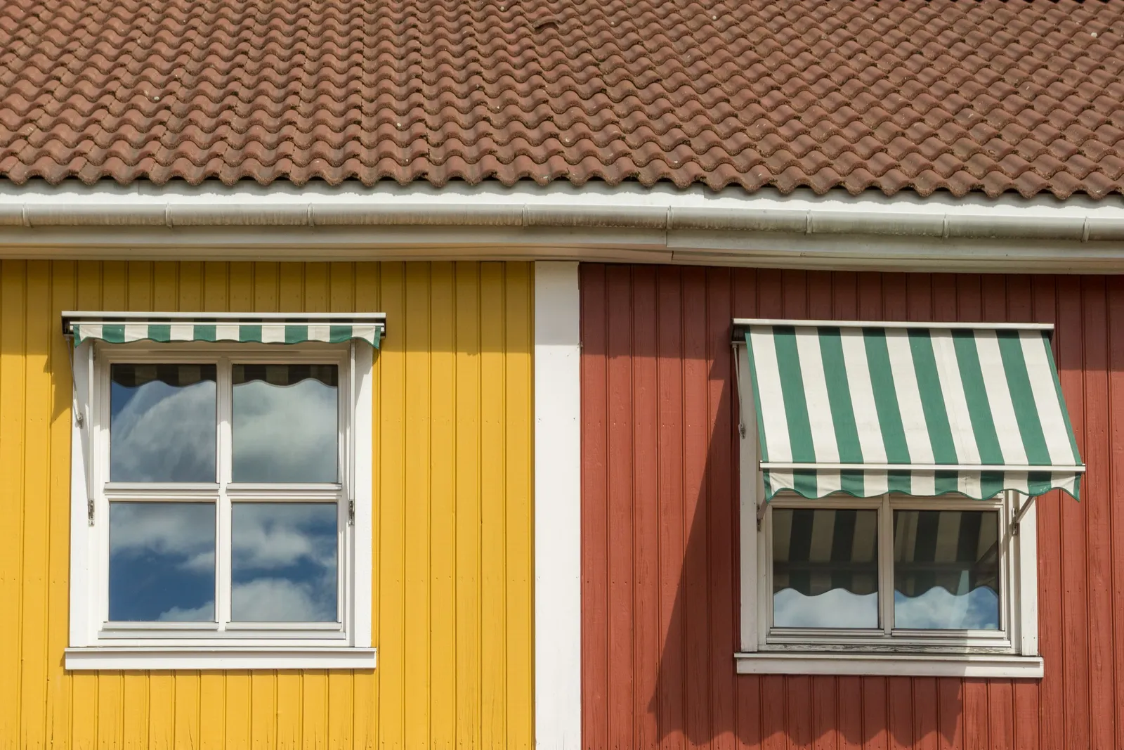 Grönrandig fönstermarkis över ett spröjsat fönster på ett rött trähus