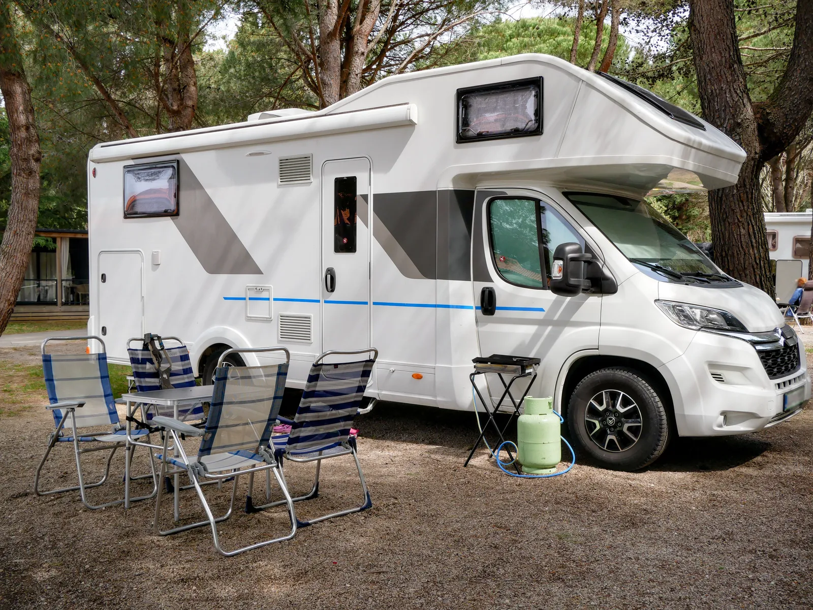 Husbil på en camping i skogen med campingmöbler bredvid