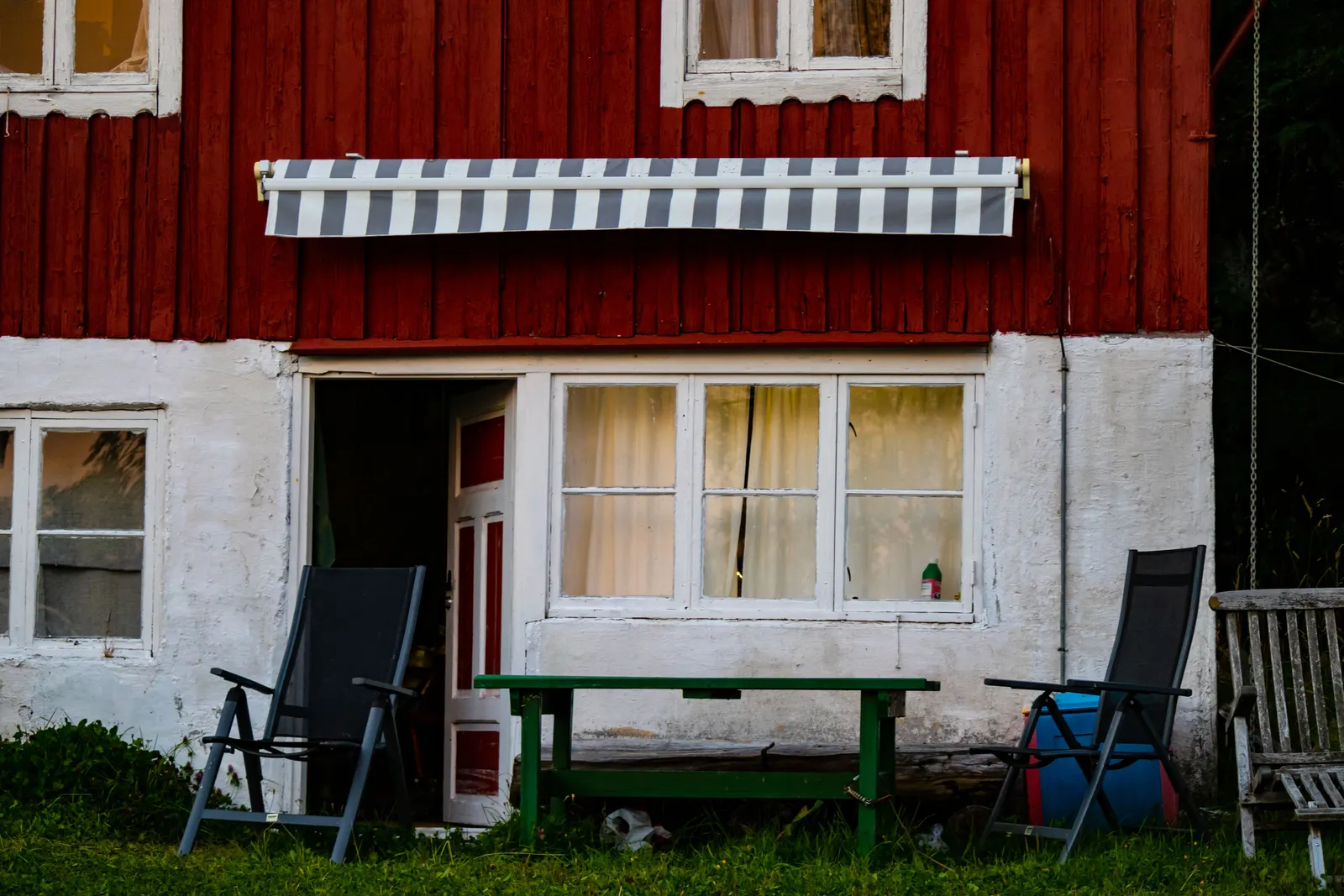 Rött trähus med randig markis över entrén och en enkel uteplats framför